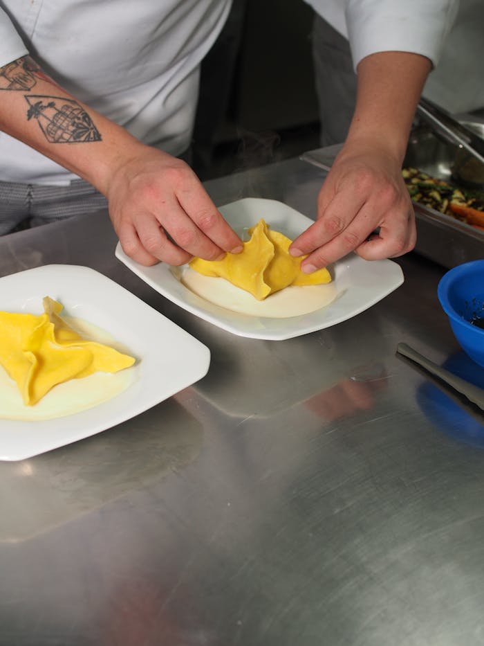 Chef's hands carefully plating fresh ravioli in a professional kitchen setting.